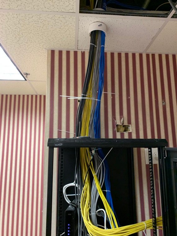 Dressed cable bundle dropping from a ceiling pass-through into a network rack